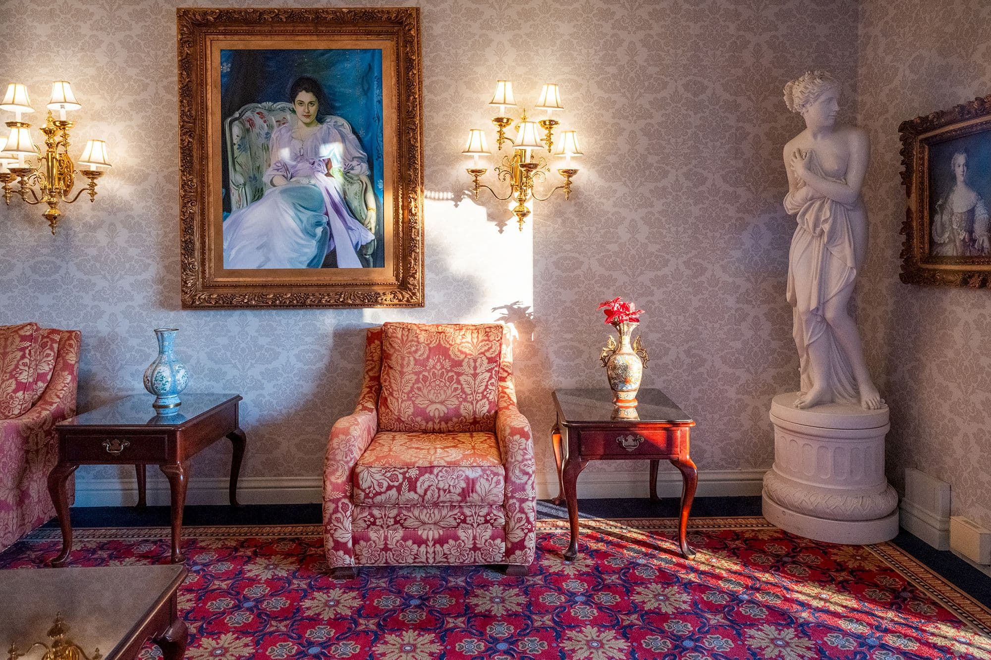 Sunlit parlor with a damask armchair, brass sconces and a gilt-framed portrait