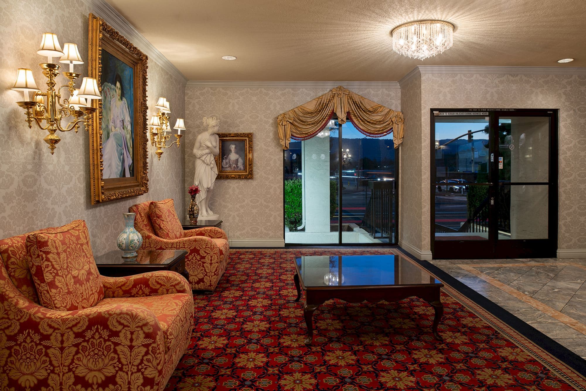 Lobby lounge with damask armchairs, a crystal ceiling light and glass doors to the street