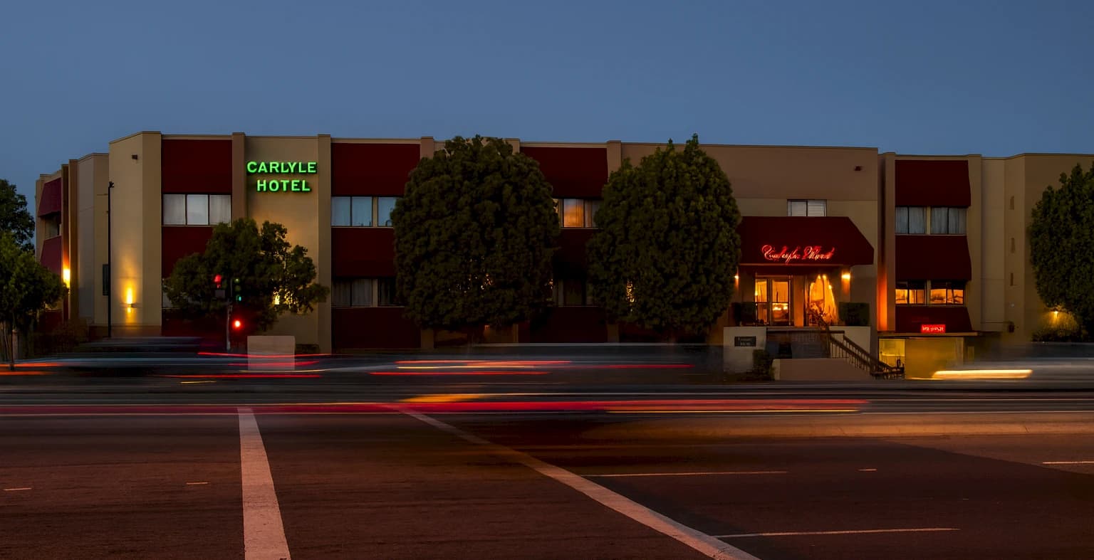 The Carlyle Hotel at dusk, its sign lit and traffic streaking past