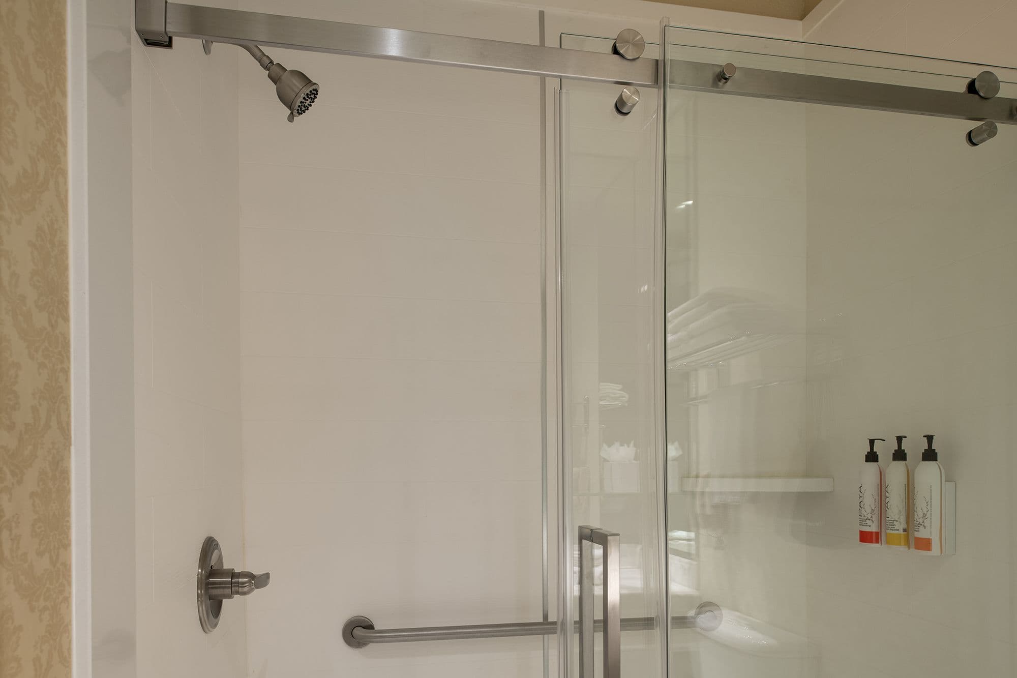 Walk-in shower with a sliding glass door and a stainless steel grab bar
