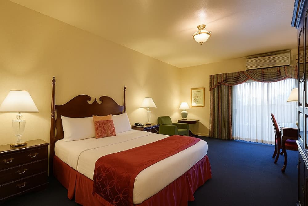 King guest room with a carved headboard, armchair, armoire and a writing desk by the window